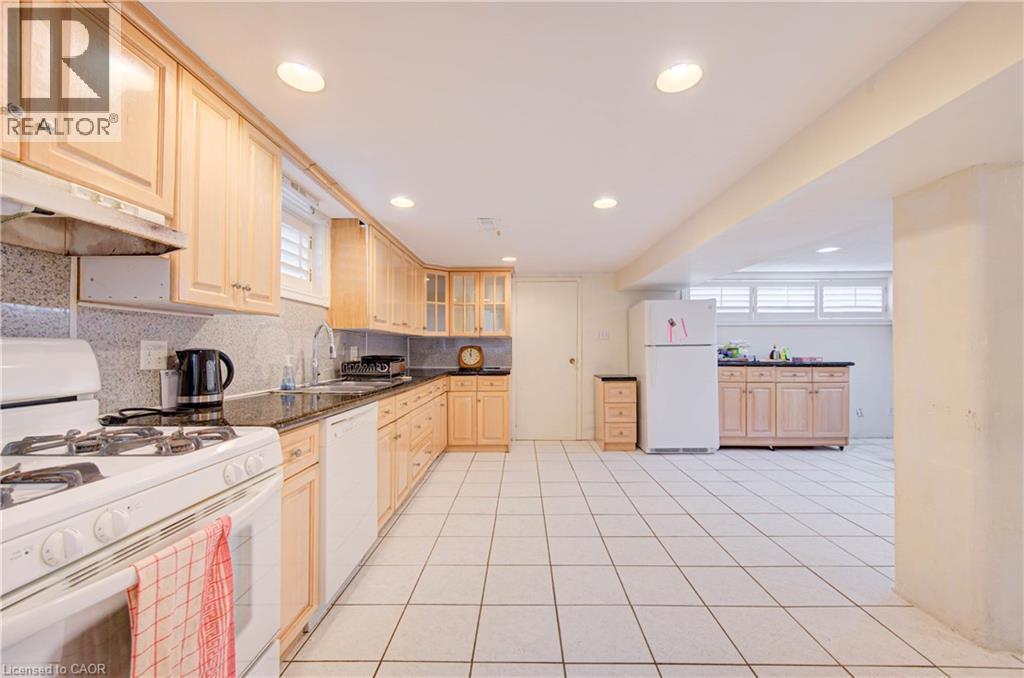 Spacious kitchen with a white tile floor, ample wood cabinetry, dark countertops, and a white gas range - 465 Herkimer Street, Hamilton, ON