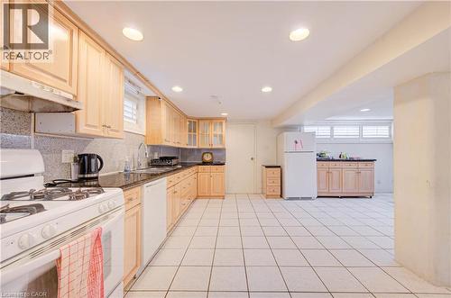Spacious kitchen with a white tile floor, ample wood cabinetry, dark countertops, and a white gas range - 465 Herkimer Street, Hamilton, ON 