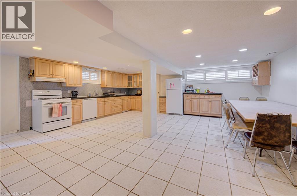 Spacious open-concept kitchen and dining area featuring wood-finish cabinetry, stainless steel appliances, ceramic tile flooring throughout, recessed ceiling lighting, and abundant natural light from - 465 Herkimer Street, Hamilton, ON