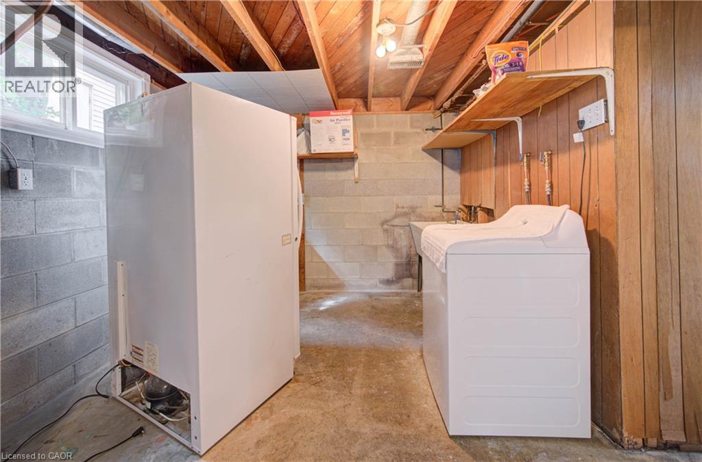 Unfinished basement with exposed ceiling joists, concrete block walls, a single window, and a utility sink - 465 Herkimer Street, Hamilton, ON