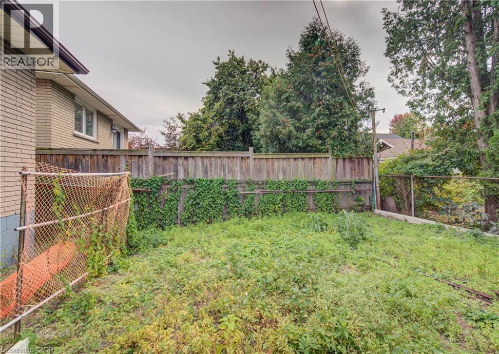 Fenced backyard with mature perimeter trees, a wood privacy fence, and brick exterior - 465 Herkimer Street, Hamilton, ON