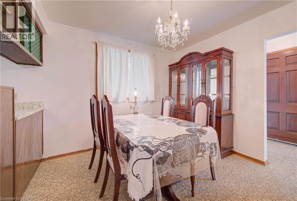 Dining area featuring a crystal chandelier, patterned flooring, and an adjacent wood-paneled door - 465 Herkimer Street, Hamilton, ON