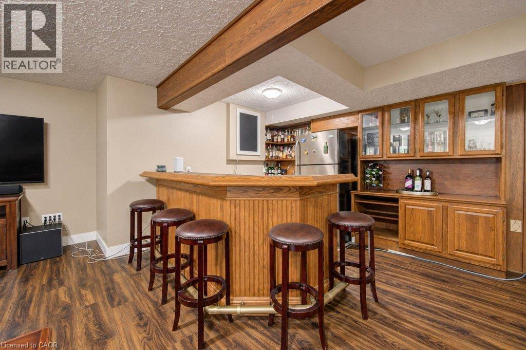 Wood-finish flooring, built-in wooden bar with foot rail, wood cabinetry with glass-front uppers, stainless steel refrigerator, and recessed lighting - 1370 Thorman Place, Cambridge, ON