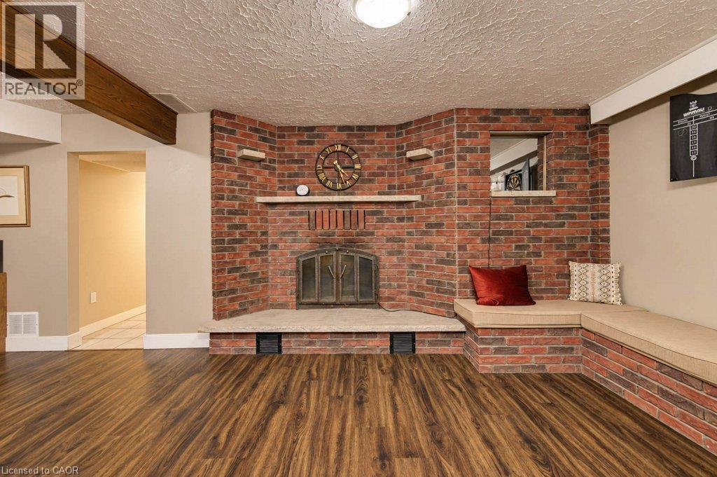 Brick fireplace with hearth, built-in corner seating, wood-finish flooring, and exposed ceiling beam - 1370 Thorman Place, Cambridge, ON