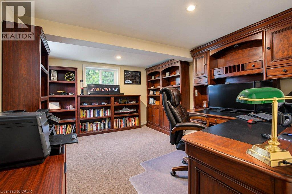 Sophisticated home office featuring rich wood-finish cabinetry, built-in shelving with display storage, desk workspace with task lighting, plush seating, and carpet flooring - 1370 Thorman Place, Cambridge, ON