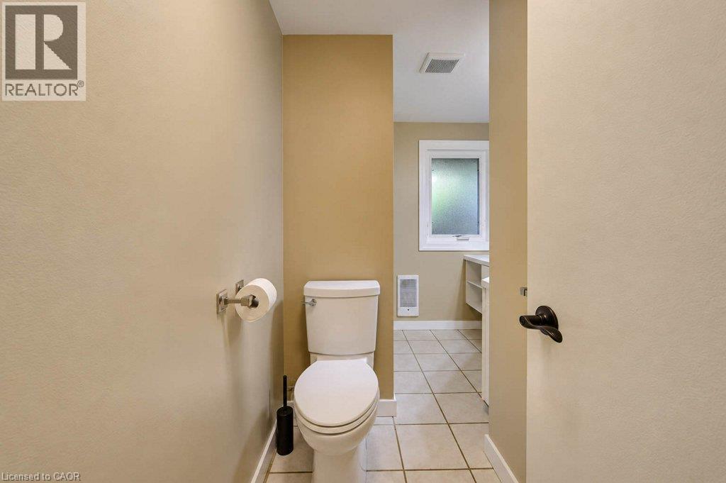 White toilet with tiled flooring, neutral wall tones, and an opaque window - 1370 Thorman Place, Cambridge, ON