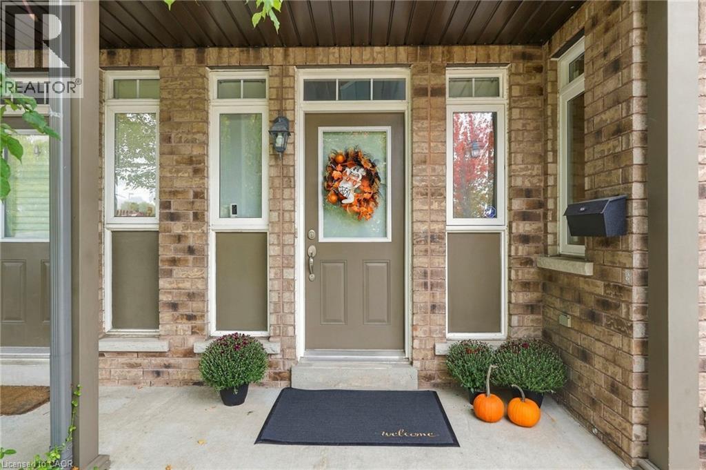 Brick façade with a covered front porch, featuring a panel-style entry door and flanking sidelight windows with transom details - 1076 Ryckman Common, Burlington, ON