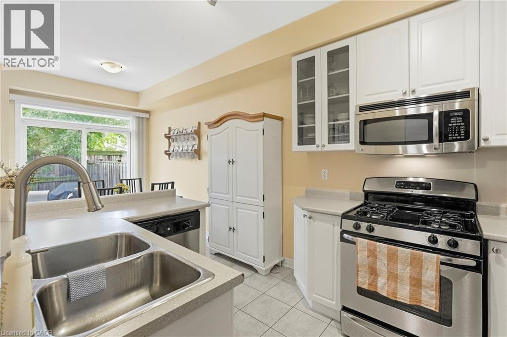 Kitchen featuring white cabinetry, stainless steel appliances, a double basin sink with a high-arch faucet, and light-toned countertops - 1076 Ryckman Common, Burlington, ON