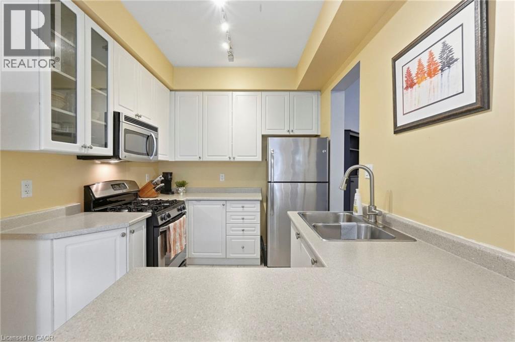 Contemporary kitchen featuring white cabinetry, stainless steel appliances, light-toned countertops and a double basin sink - 1076 Ryckman Common, Burlington, ON