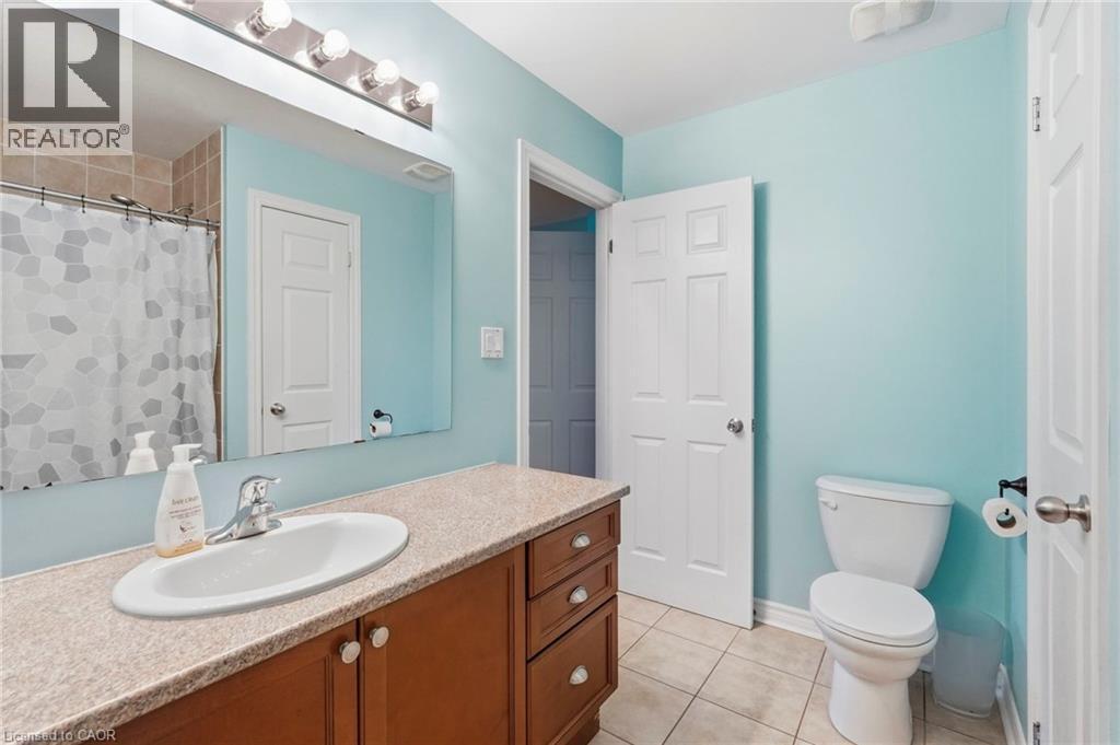 Bathroom featuring a vanity with an integrated sink, wood-finish cabinetry, a large mirror, and tiled flooring - 1076 Ryckman Common, Burlington, ON