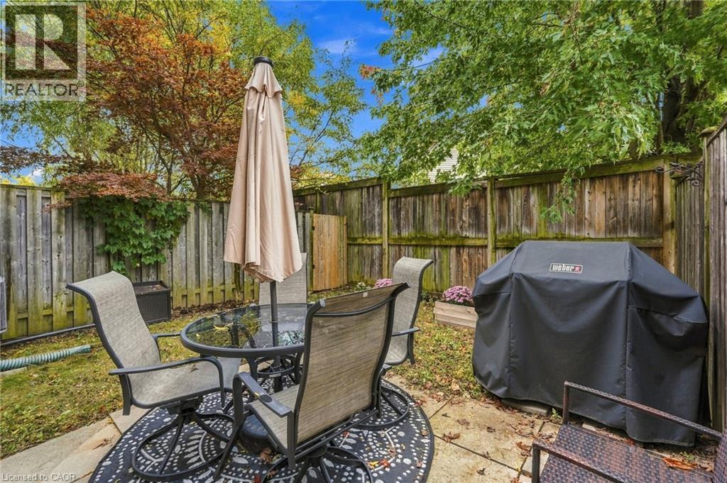 Patio area featuring a paved surface, wooden fencing, and mature trees - 1076 Ryckman Common, Burlington, ON