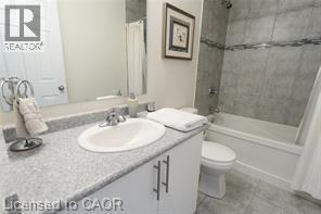 Vanity with a speckled countertop and integrated sink, chrome faucet, white cabinetry with dark pull handles, and a white bathtub with subway tile surround and decorative accent band - 28 Madonna Drive, Hamilton, ON
