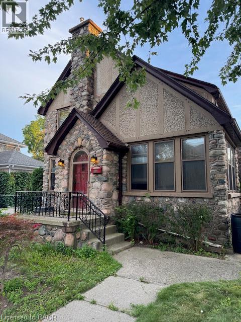 Stone and stucco exterior featuring a prominent stone chimney, arched doorway, and dark-framed windows - 255 Main Street, Cambridge, ON