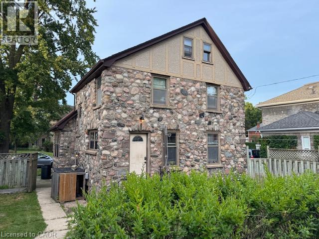 Stone-clad exterior with multiple windows, an arched entry door, and a peaked roofline with decorative detailing - 255 Main Street, Cambridge, ON