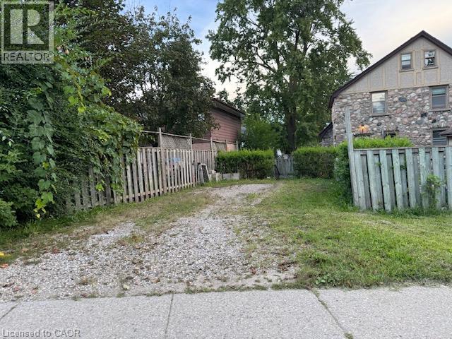 Gravel driveway with a wooden picket fence and mature landscaping - 255 Main Street, Cambridge, ON