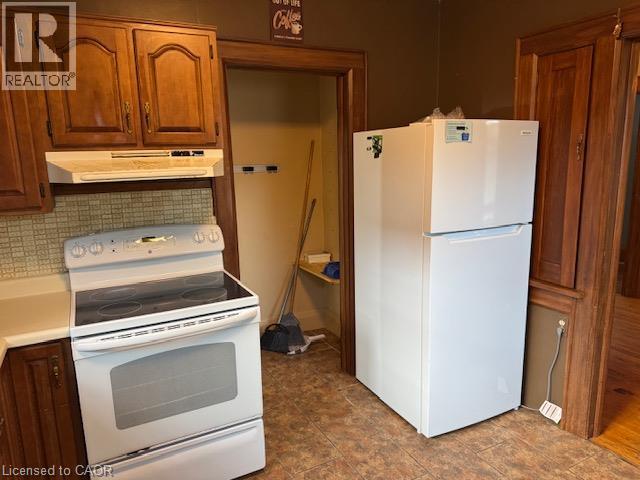 Wood-finish upper and lower cabinetry, white electric range with overhead ventilation, white refrigerator, and tiled flooring - 255 Main Street, Cambridge, ON
