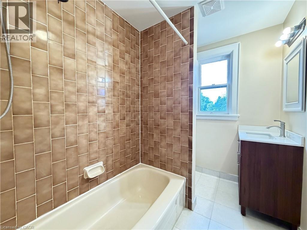 Tiled shower surround, built-in tub, single window, vanity with integrated sink, and wall-mounted light fixture - 507 Aberdeen Avenue, Hamilton, ON