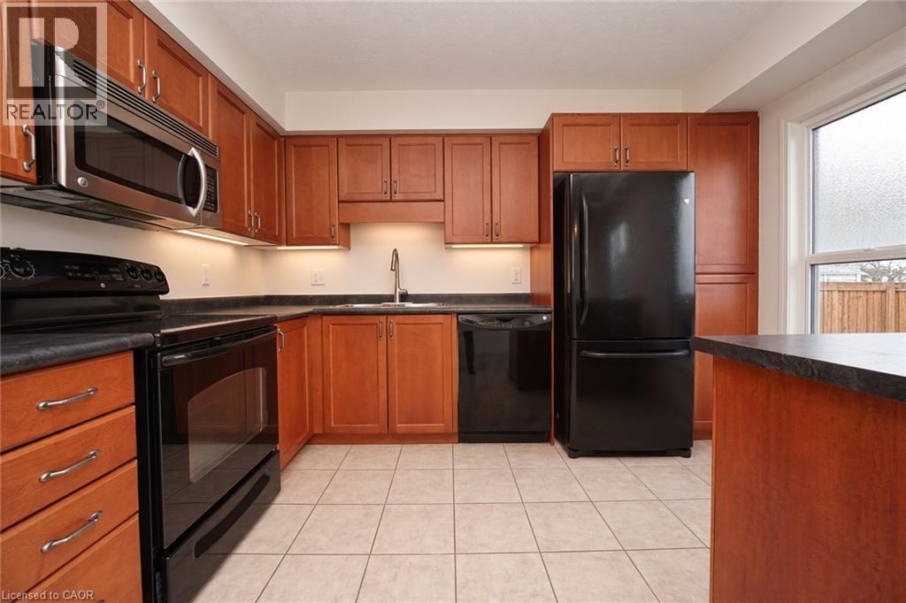 Wood-finish cabinetry with silver-tone hardware, stainless steel microwave, black range, integrated black dishwasher, and black refrigerator - 250 Parkvale Drive, Kitchener, ON