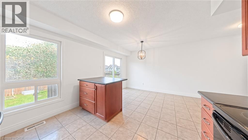 Tile flooring, white walls, kitchen island with dark countertop, pendant light fixture, and sliding glass door - 250 Parkvale Drive, Kitchener, ON