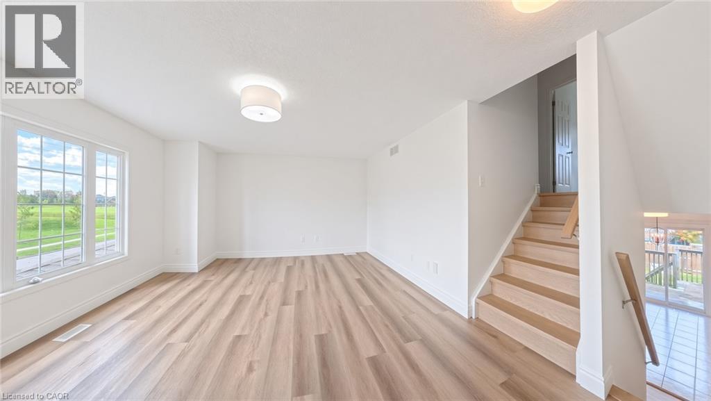 Light wood-finish flooring, white walls, large window with grid pattern, neutral ceiling light fixture, and a wood staircase with railing - 250 Parkvale Drive, Kitchener, ON