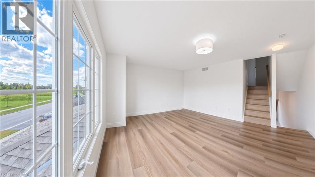 Large multipane windows, wood-finish flooring, two ceiling-mounted light fixtures, and a wooden staircase with railing - 250 Parkvale Drive, Kitchener, ON