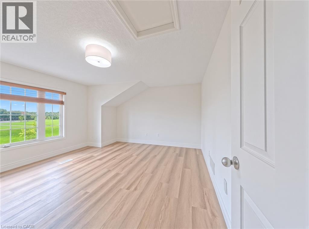 Expansive room featuring wood-finish flooring, a contemporary ceiling light fixture, a large window, and a white paneled door - 250 Parkvale Drive, Kitchener, ON