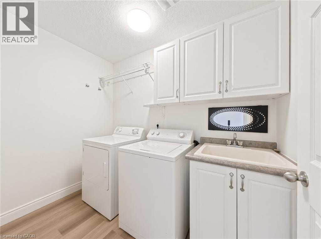 Laundry room with wood-finish flooring, white cabinetry, utility sink, and overhead wire shelving - 250 Parkvale Drive, Kitchener, ON