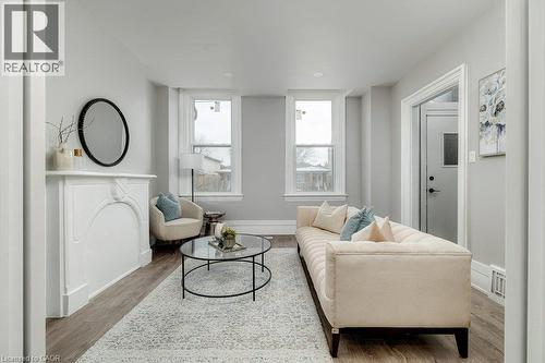Bright living space featuring wood-finish flooring, a decorative fireplace mantel, and two large windows - 125 Cathcart Street, Hamilton, ON 