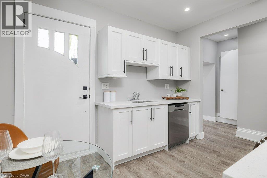 White shaker-style cabinetry with matte black hardware, stainless steel dishwasher, light-toned wood-finish flooring, and a solid surface countertop - 125 Cathcart Street, Hamilton, ON