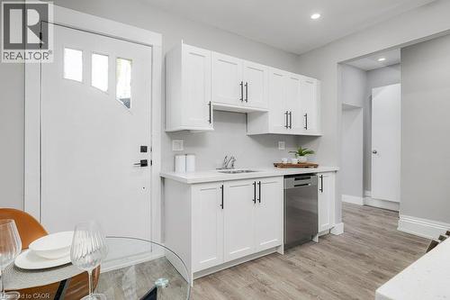 White shaker-style cabinetry with matte black hardware, stainless steel dishwasher, light-toned wood-finish flooring, and a solid surface countertop - 125 Cathcart Street, Hamilton, ON 