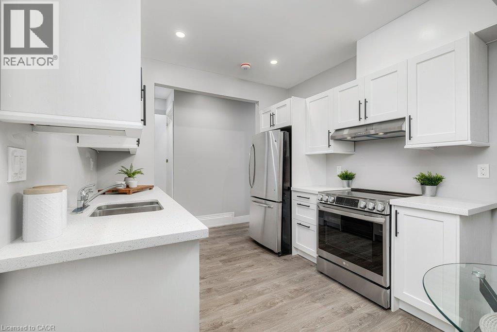 Kitchen featuring white shaker-style cabinetry, stainless steel appliances, light-toned countertops, and wood-finish flooring - 125 Cathcart Street, Hamilton, ON