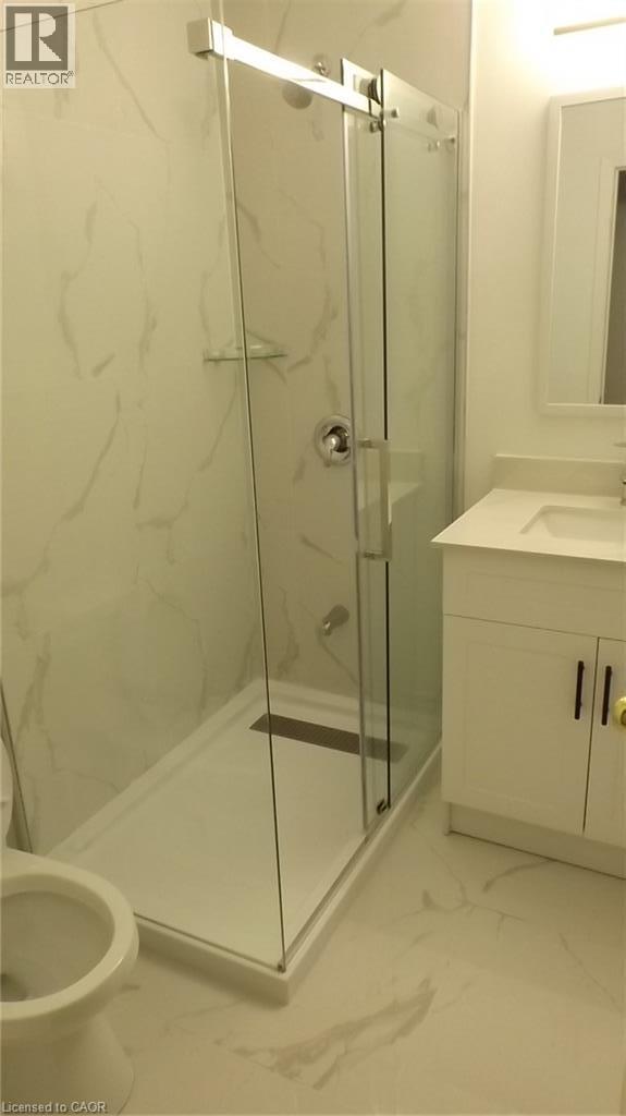 Glass-enclosed shower with a linear drain, white vanity with a white countertop and rectangular sink, and white wall and floor tiling - 68 Austin Drive, Waterloo, ON