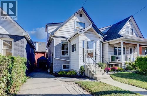 White siding exterior with a gabled roofline, front porch, concrete steps with metal railings, and a paved driveway - 3 Craigmiller Avenue, Hamilton, ON 