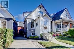 White siding exterior with a gabled roofline, front porch, concrete steps with metal railings, and a paved driveway -