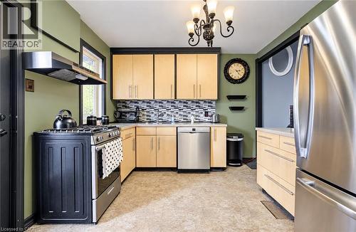 Kitchen featuring light wood-finish cabinetry, stainless steel appliances, a mosaic tile backsplash, and a corner sink - 3 Craigmiller Avenue, Hamilton, ON 