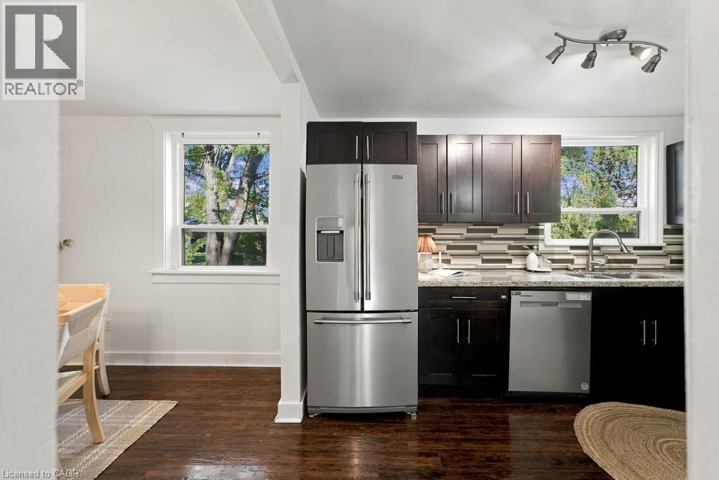 Kitchen with stainless steel appliances, dark wood-finish cabinetry, granite-style countertops, and mosaic tile backsplash - 284 East 21St Street, Hamilton, ON