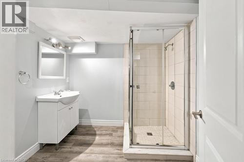 Walk-in shower with clear glass enclosure and subway tile surround, white vanity with integrated sink, wood-finish flooring, and wall-mounted vanity lighting - 284 East 21St Street, Hamilton, ON 
