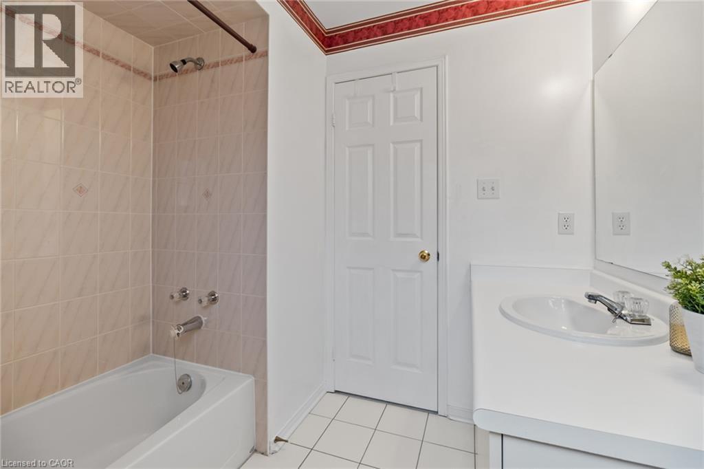 White tile flooring, white vanity with integrated sink, chrome faucet, wall-mounted mirror, and a bathtub with tile surround - 1263 Bantham Street, Mississauga, ON