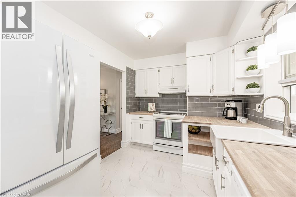 Bright kitchen featuring white cabinetry, wood-finish countertops, subway tile backsplash, a white undermount sink, and a stainless steel faucet - 388 Appleby Line, Burlington, ON