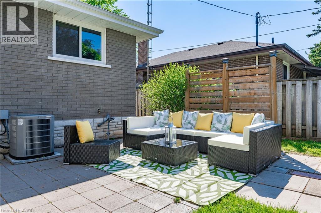 Paved patio area, brick exterior, white window trim, wooden privacy fence, green lawn - 388 Appleby Line, Burlington, ON