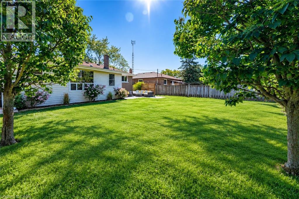 Expansive green lawn with mature trees, a white-sided residence featuring large windows, and a privacy fence - 388 Appleby Line, Burlington, ON