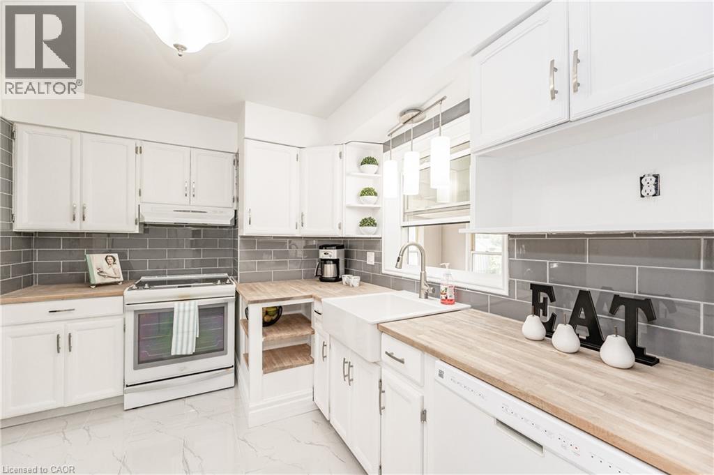 White cabinetry with brushed nickel hardware, light wood-finish countertops, gray subway tile backsplash, white farmhouse sink, and white appliances - 388 Appleby Line, Burlington, ON