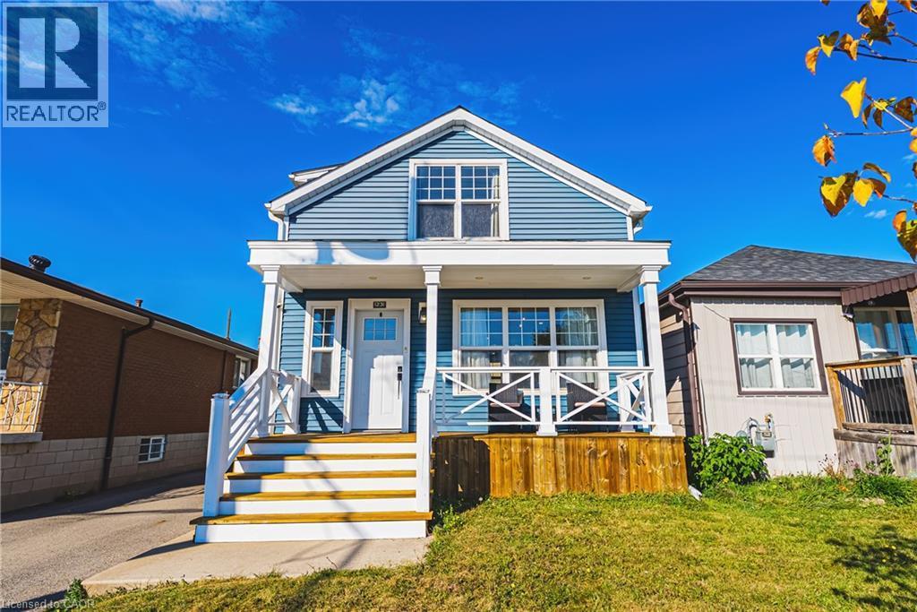Blue siding exterior, white trim accents, prominent front porch with white railing, wood stairs, and a front yard with natural grass - 1231 Dunsmure Road, Hamilton, ON
