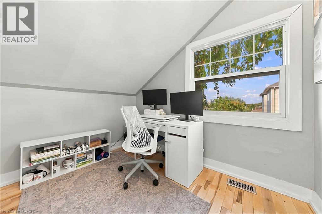 Sloped ceiling room featuring a large window, light wood-finish flooring, and a built-in white shelving unit - 1231 Dunsmure Road, Hamilton, ON