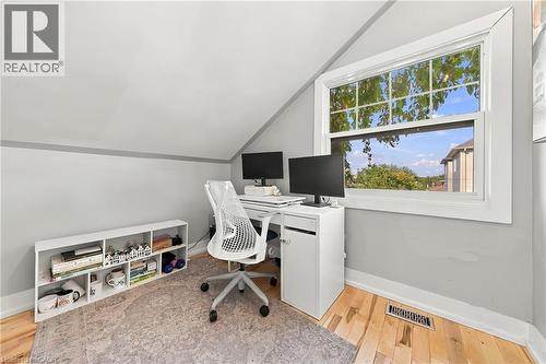 Sloped ceiling room featuring a large window, light wood-finish flooring, and a built-in white shelving unit - 1231 Dunsmure Road, Hamilton, ON 