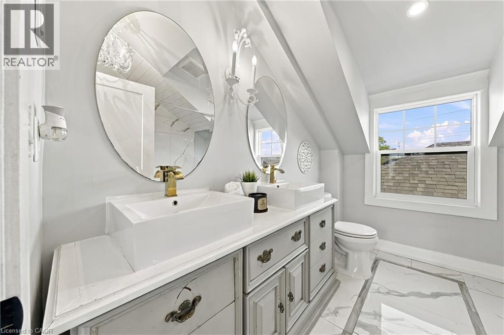 Dual vessel sinks with gold-tone hardware, oval mirrors, and a multi-pane window - 1231 Dunsmure Road, Hamilton, ON