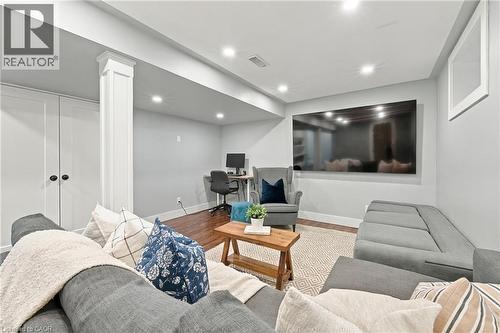 Recessed lighting illuminates this room featuring wood-finish flooring, a built-in desk area, and a wall-mounted media screen - 1231 Dunsmure Road, Hamilton, ON 