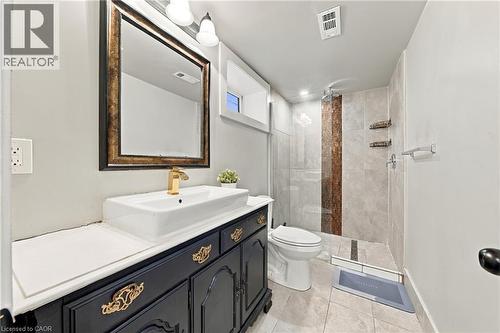 Vanity with a vessel sink and gold-finish faucet, framed mirror, tiled flooring, glass-enclosed shower with vertical accent tiling - 1231 Dunsmure Road, Hamilton, ON 