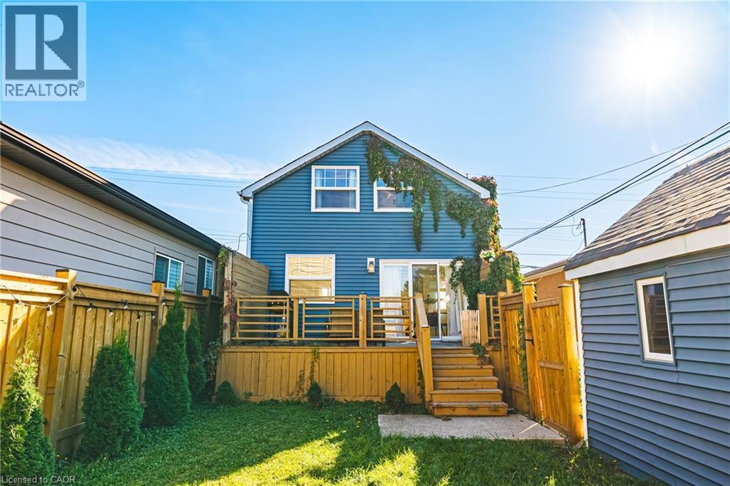 Rear exterior with blue siding, wood deck, sliding glass door, and a manicured lawn - 1231 Dunsmure Road, Hamilton, ON