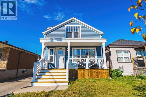 Blue siding exterior, white trim accents, prominent front porch with white railing, wood stairs, and a front yard with natural grass - 1231 Dunsmure Road, Hamilton, ON 